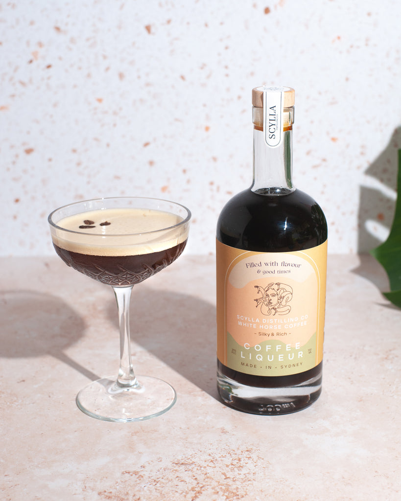 Scylla and Whitehorses cold drip coffee liqueur is shown on the right nexxt to an Espresso martini with 3 coffee beans on the left in a coupet.